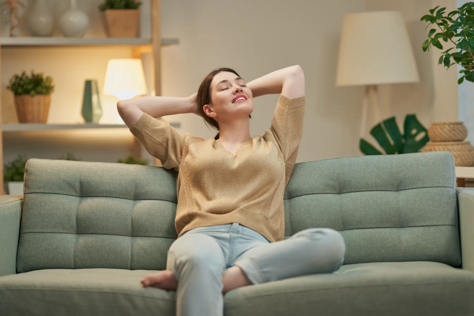A woman leaning back on her sofa with her eyes closed, smiling
