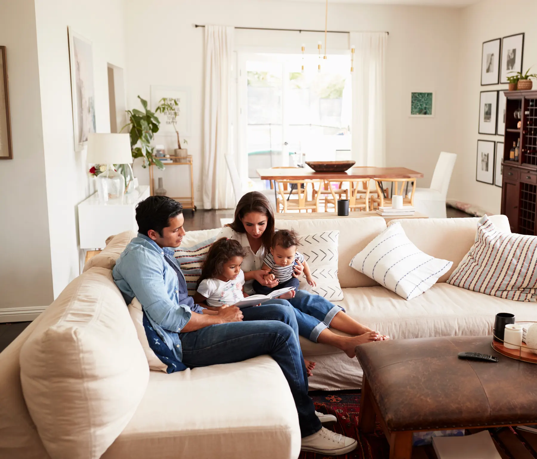 Parents reading to their two young children on a sofa in a tidy living room